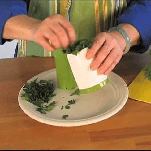 Person using a green handheld herb mill to chop fresh herbs